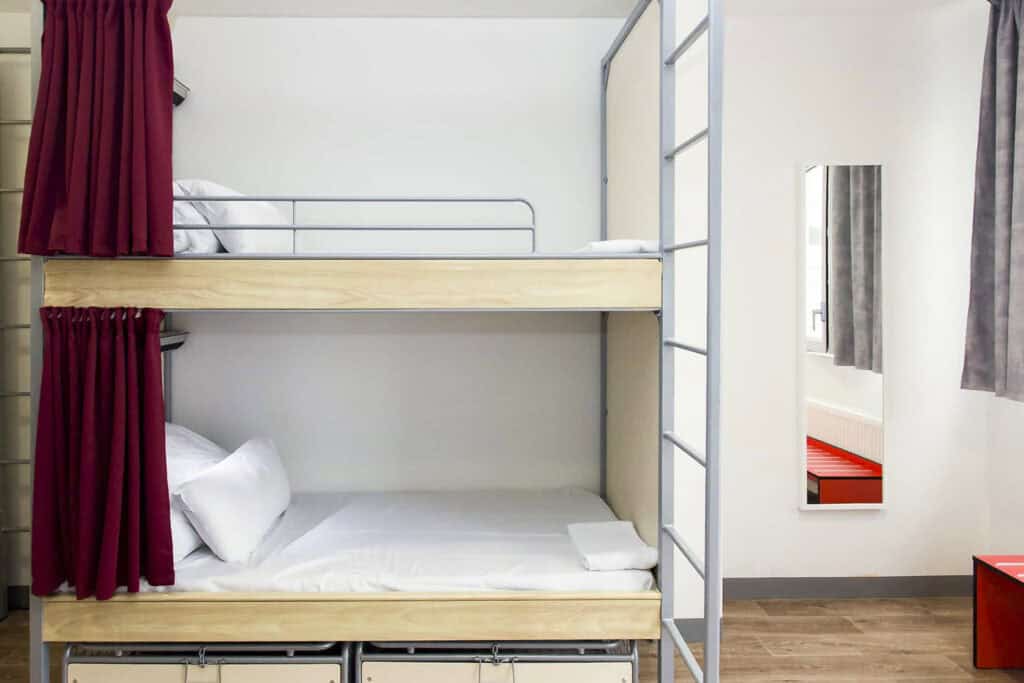 Bunk beds in a modern hostel room with white walls and red curtains.