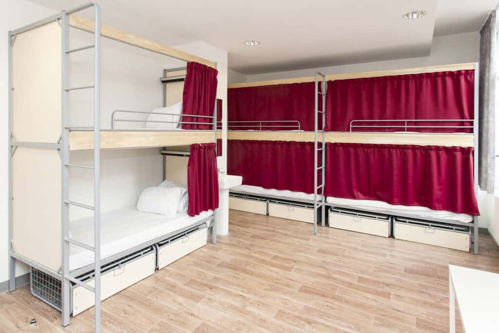 Bunk beds with red curtains in hostel dorm room.