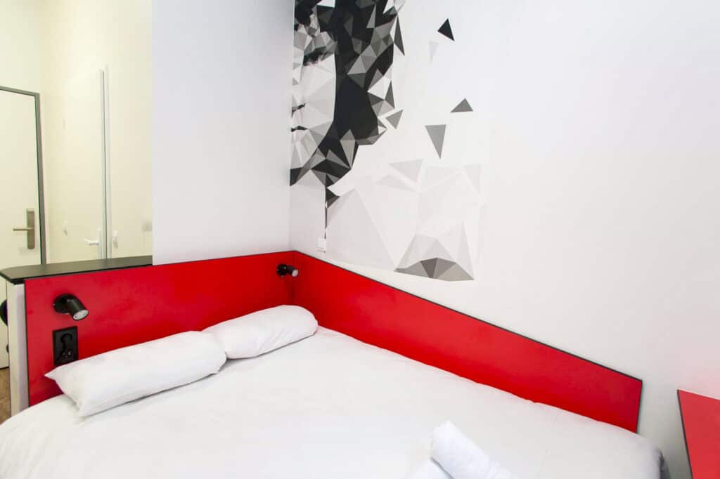 A hostel room featuring a white bed with a red headboard and contemporary wall art.