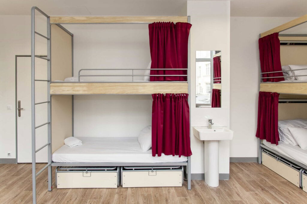 Hostel dorm room with bunk beds and red curtains at Gare du Nord, Paris.