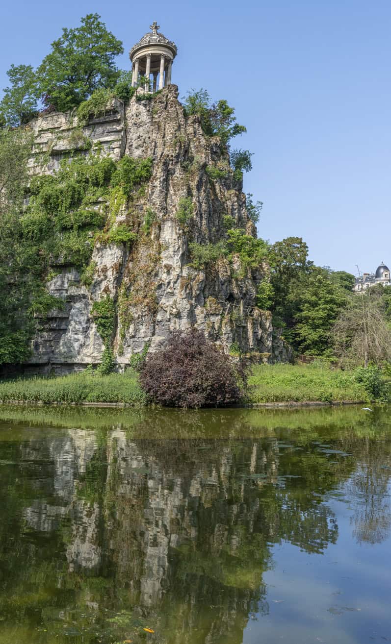 Paris, France – 06 14 2025: Buttes-Chaumont Park. View the central part of the park with belvedere island, Temple of the Sibyl, the lake, remarkable trees and vegetation