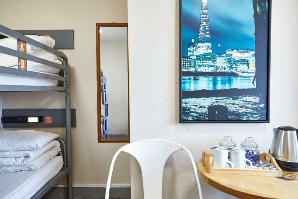 Modern hostel room with bunk beds, a white chair, and a cityscape picture on the wall.