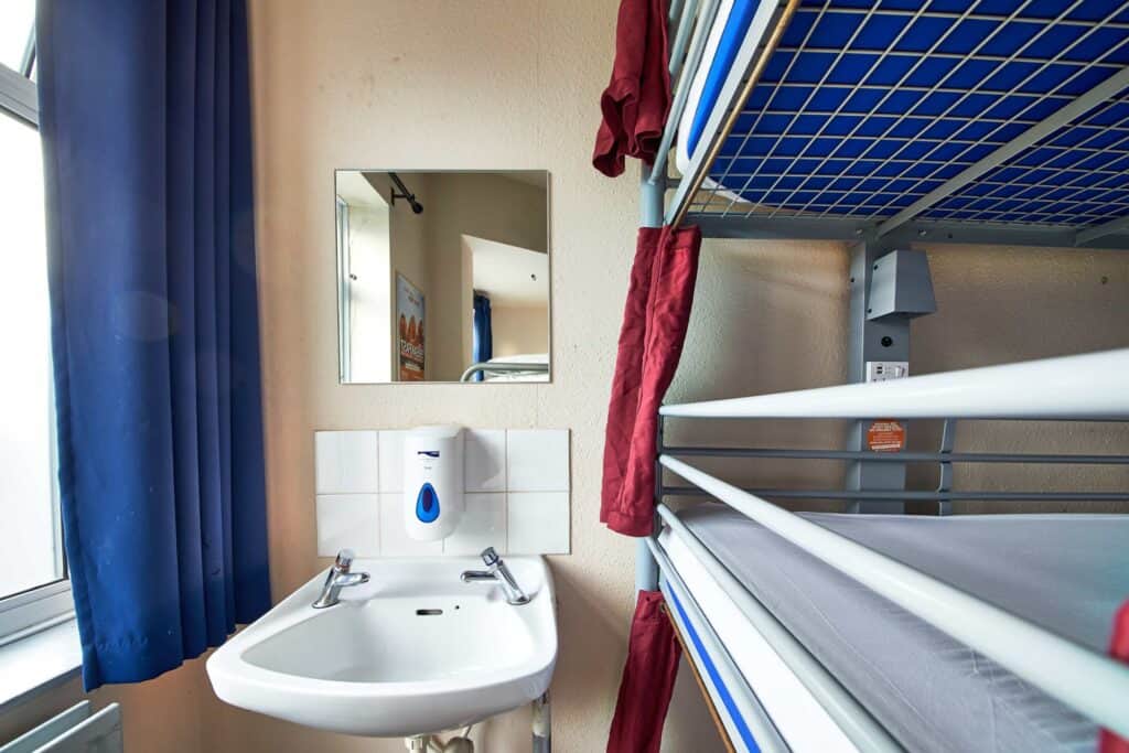 Shared dormitory bathroom with sink and bunk beds at Shepherd's Bush Hostel.