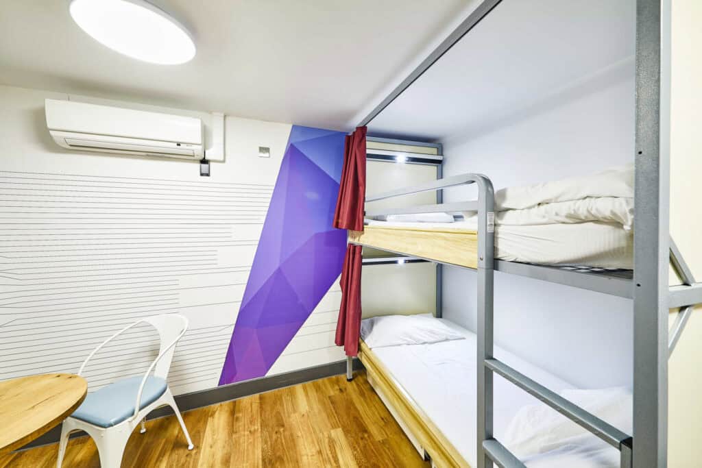 Modern hostel dorm room with bunk beds and colourful wall decor.