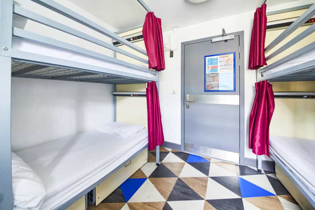 Shared dormitory room with bunk beds and red curtains at St Christopher's Shepherd's Bush.