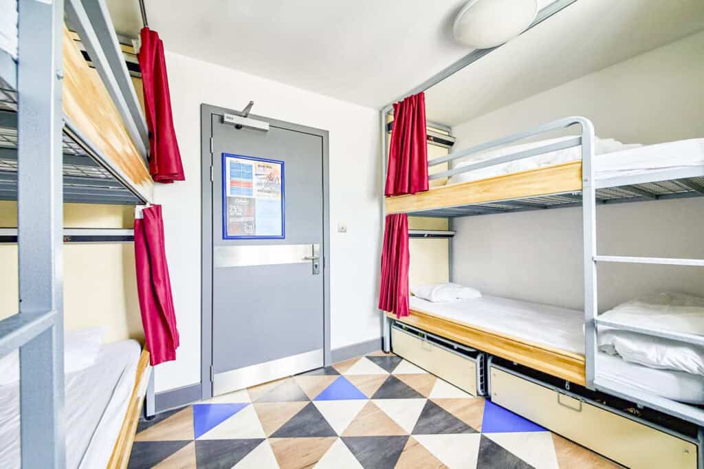 Shared dormitory room with bunk beds and red curtains at Shepherd's Bush Hostel.