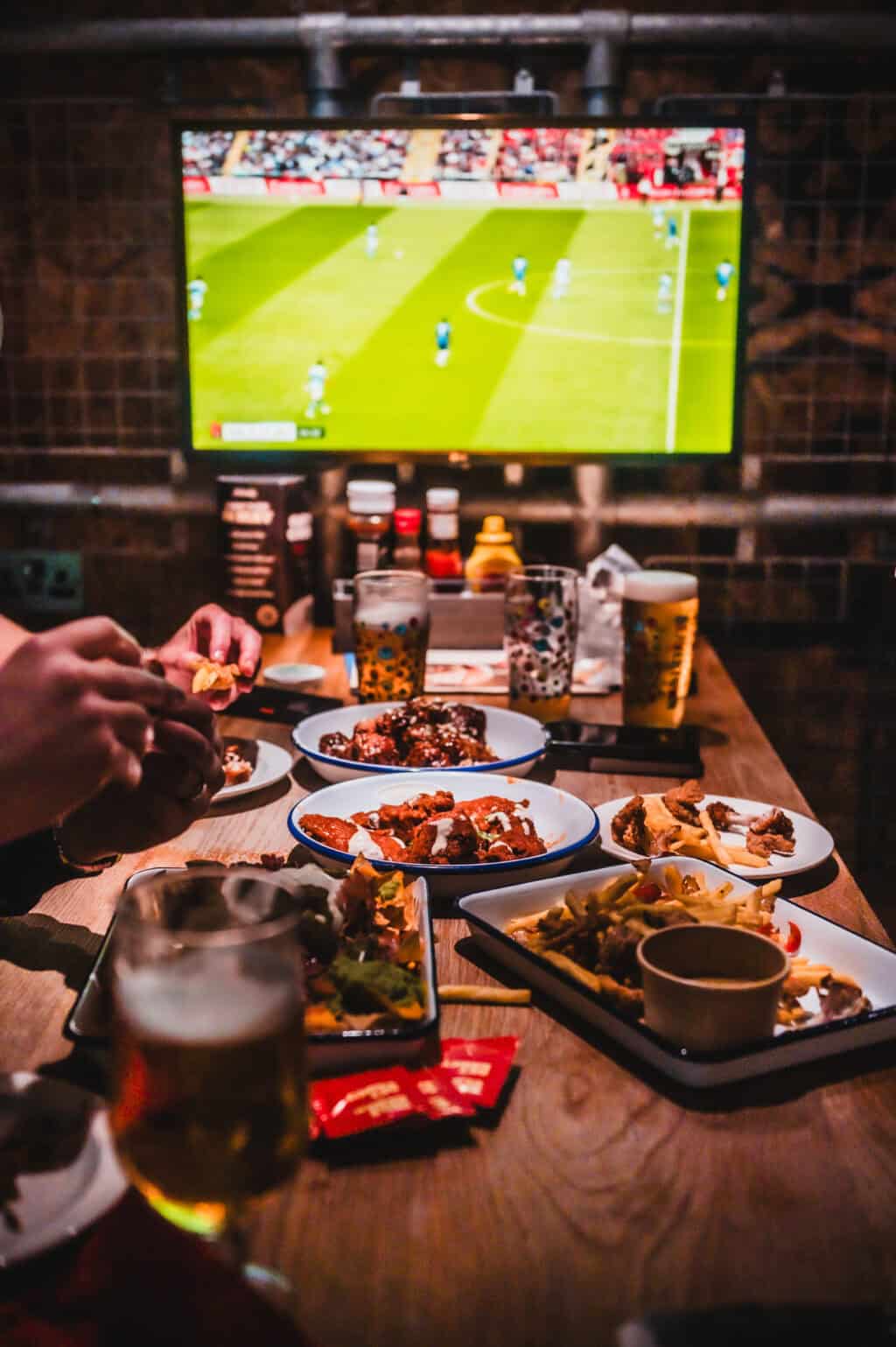 People watching a football game on TV with food and drinks at Shepherd's Bush Hostel.