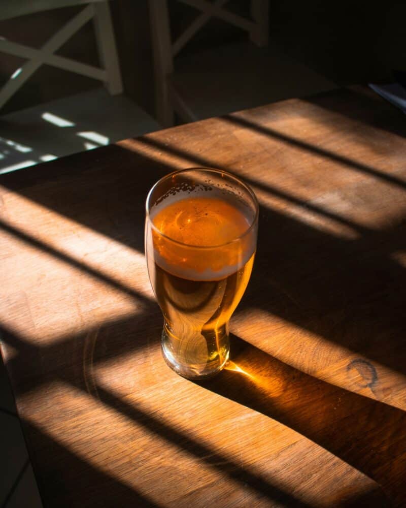 Glass of beer on a wooden table with sunlight and shadows.