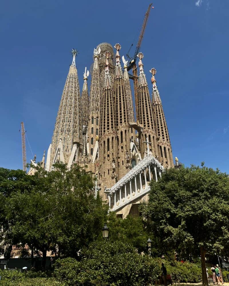 Exterior view of the Sagrada Familia with cranes and blue sky.