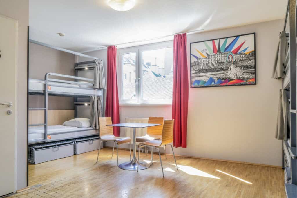 Hostel room with bunk beds, a small dining table, and colourful curtains at St Christopher’s Vienn.
