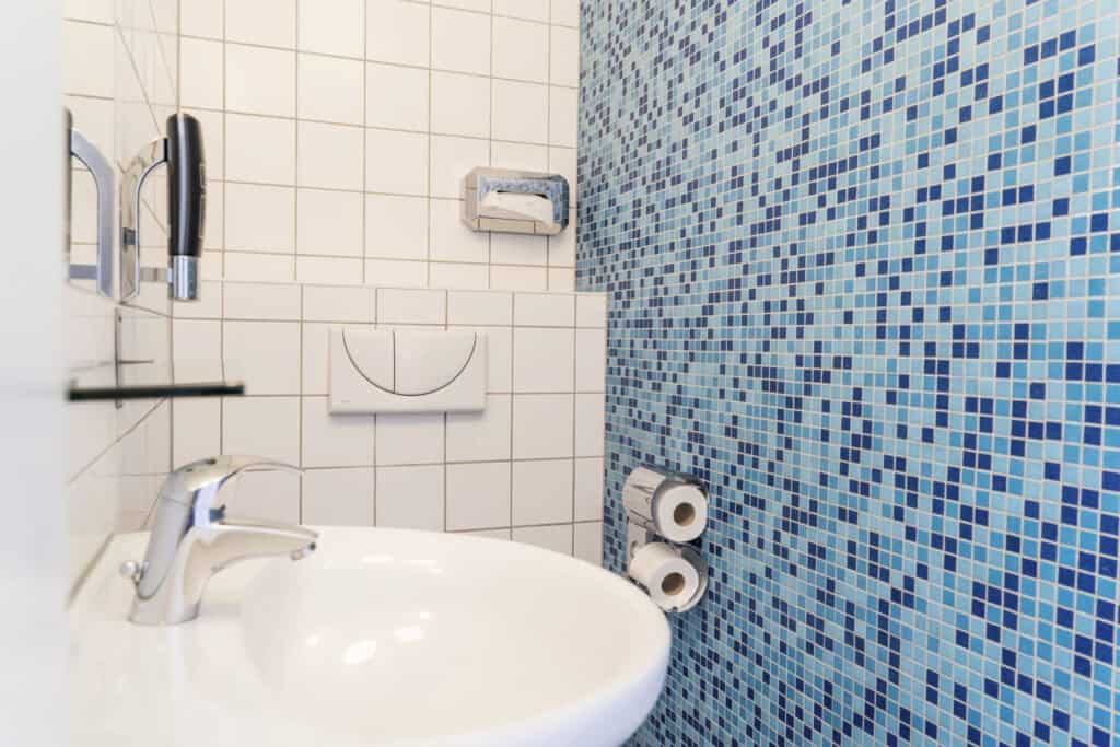 Clean hostel bathroom with blue mosaic tiles, sink, and toilet paper rolls.
