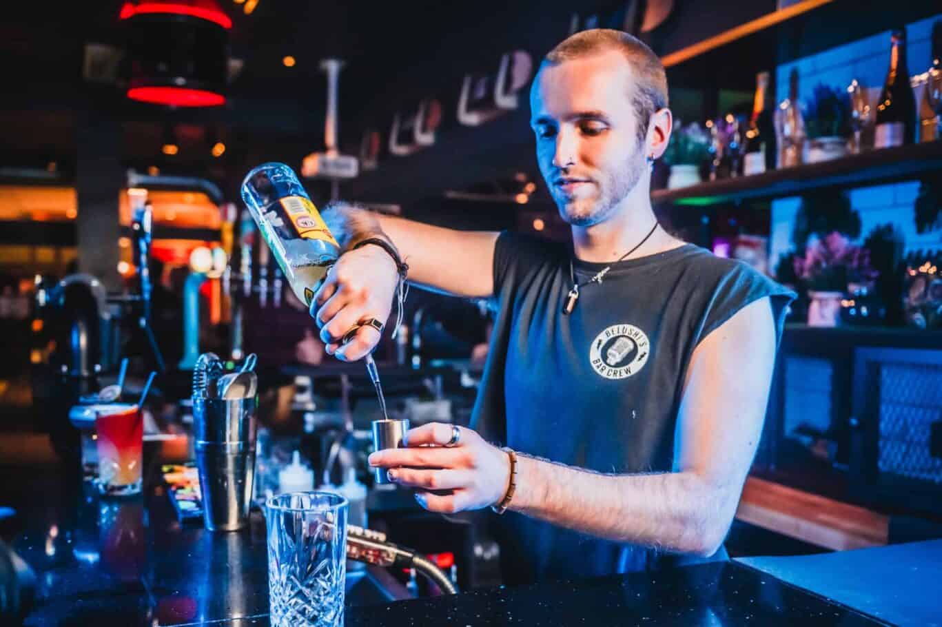 Young bartender pouring a drink at Vienna hostel bar, vibrant nightlife atmosphere.