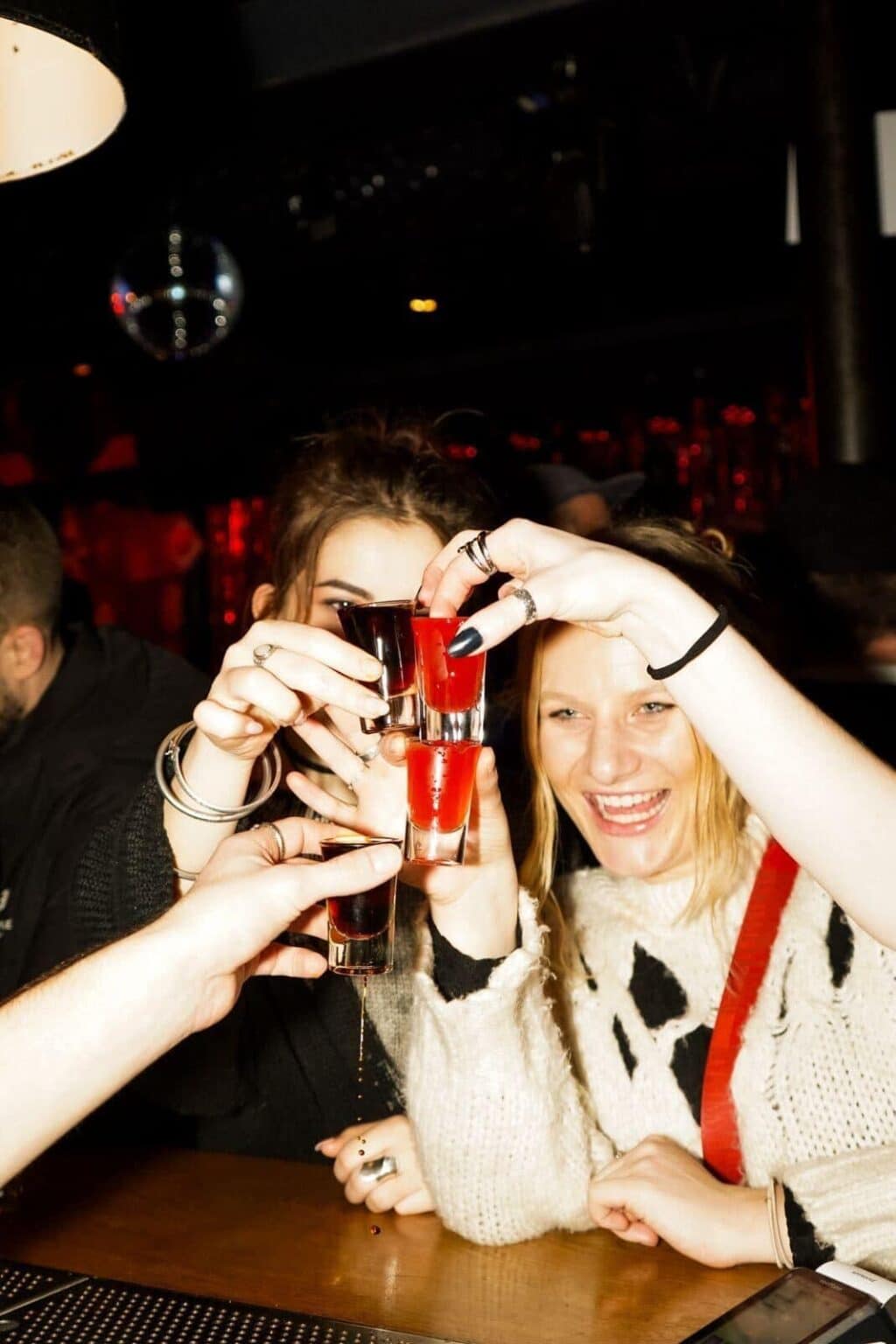 Group of friends toasting drinks at Vienna hostel bar, lively nightlife scene.