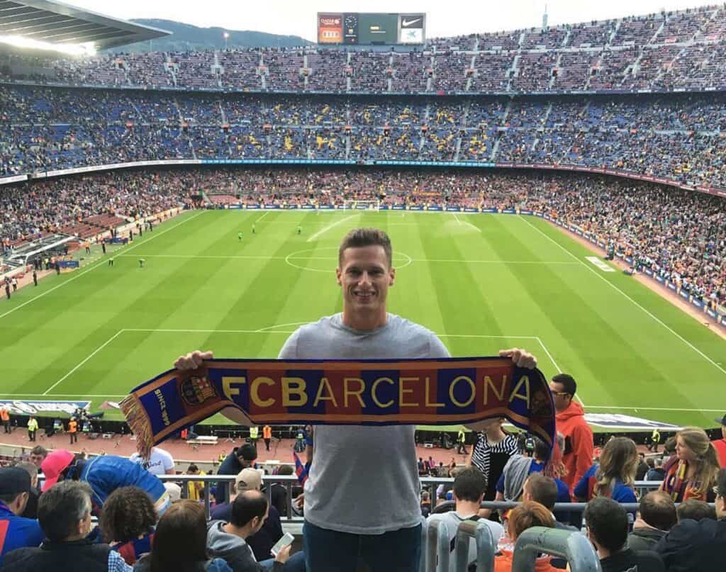 Man holding FC Barcelona scarf at a football stadium in Berlin, with a packed crowd and green pitch.