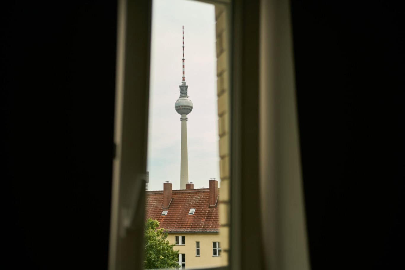 View of Berlin TV Tower through a window with curtains, showcasing cityscape and architecture.