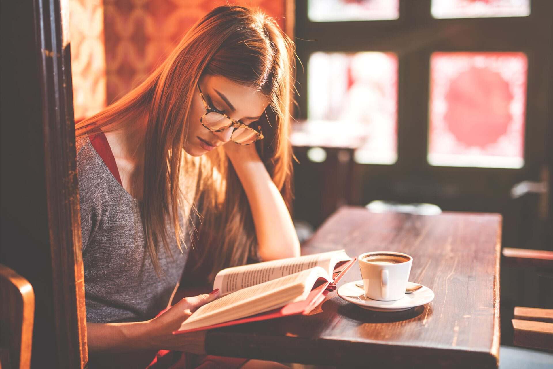 Woman reading a book at a café table with coffee, in a warm, inviting atmosphere.