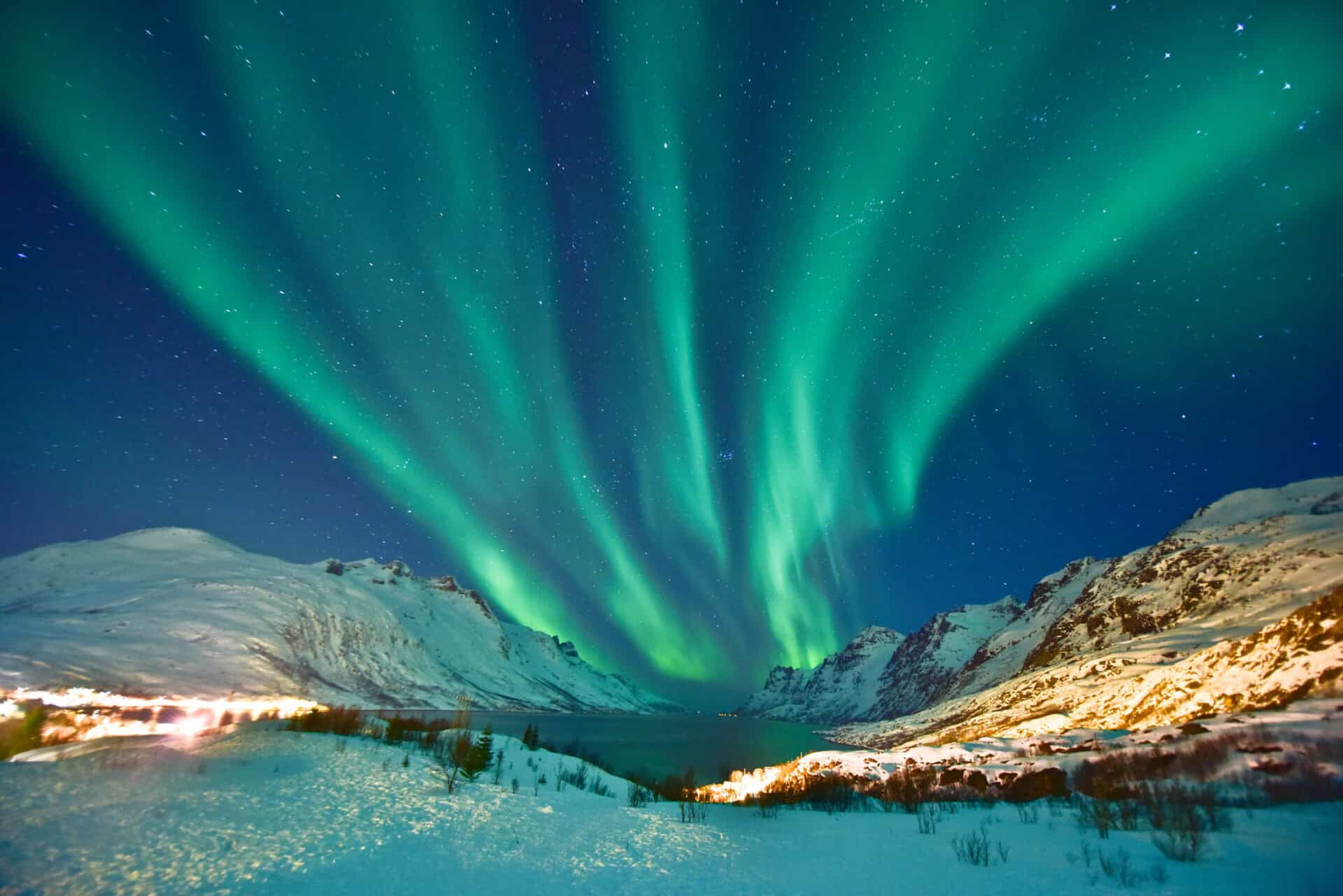 Stunning view of the Northern Lights illuminating snowy mountains in Norway at night.