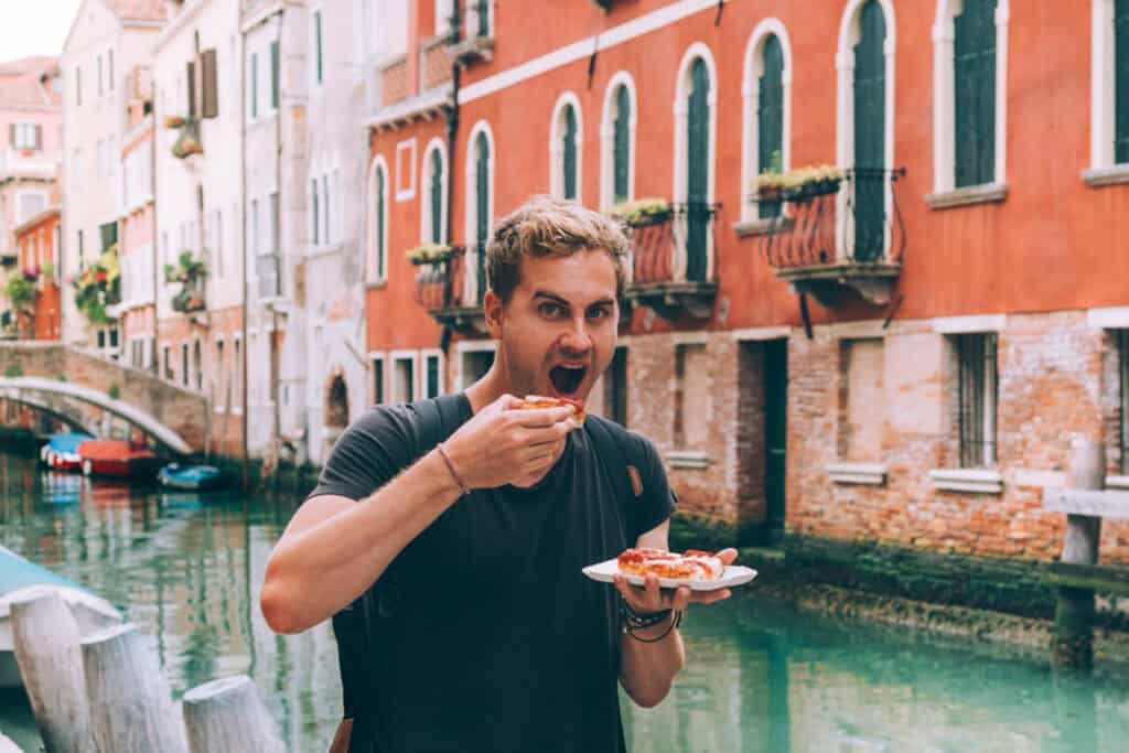 Man enjoying pizza by a canal in Venice, Italy.