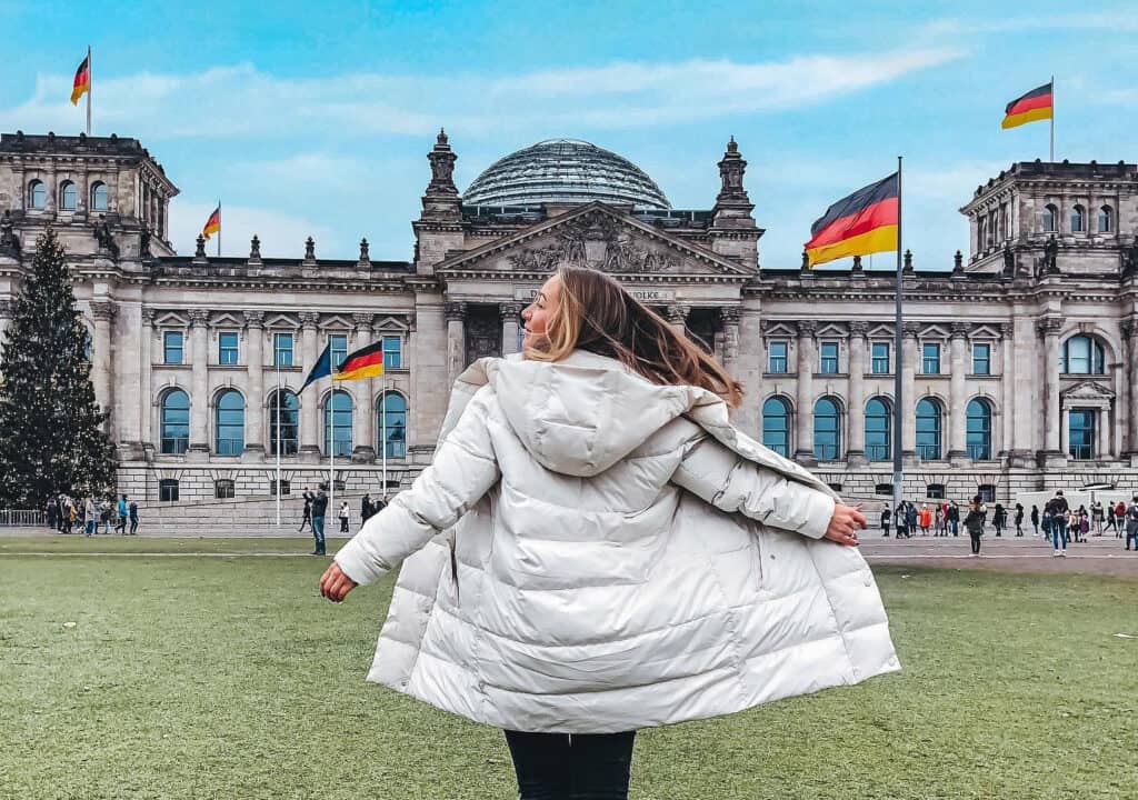 Berlin government building with flags, featuring a woman in a white coat in the foreground.