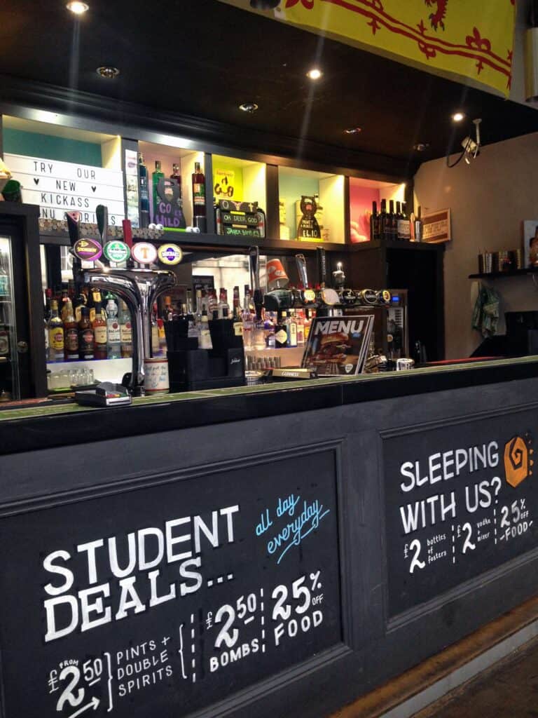 Interior view of the hostel bar at St Christopher’s Berlin - Mitte, with drinks and promotional offe.