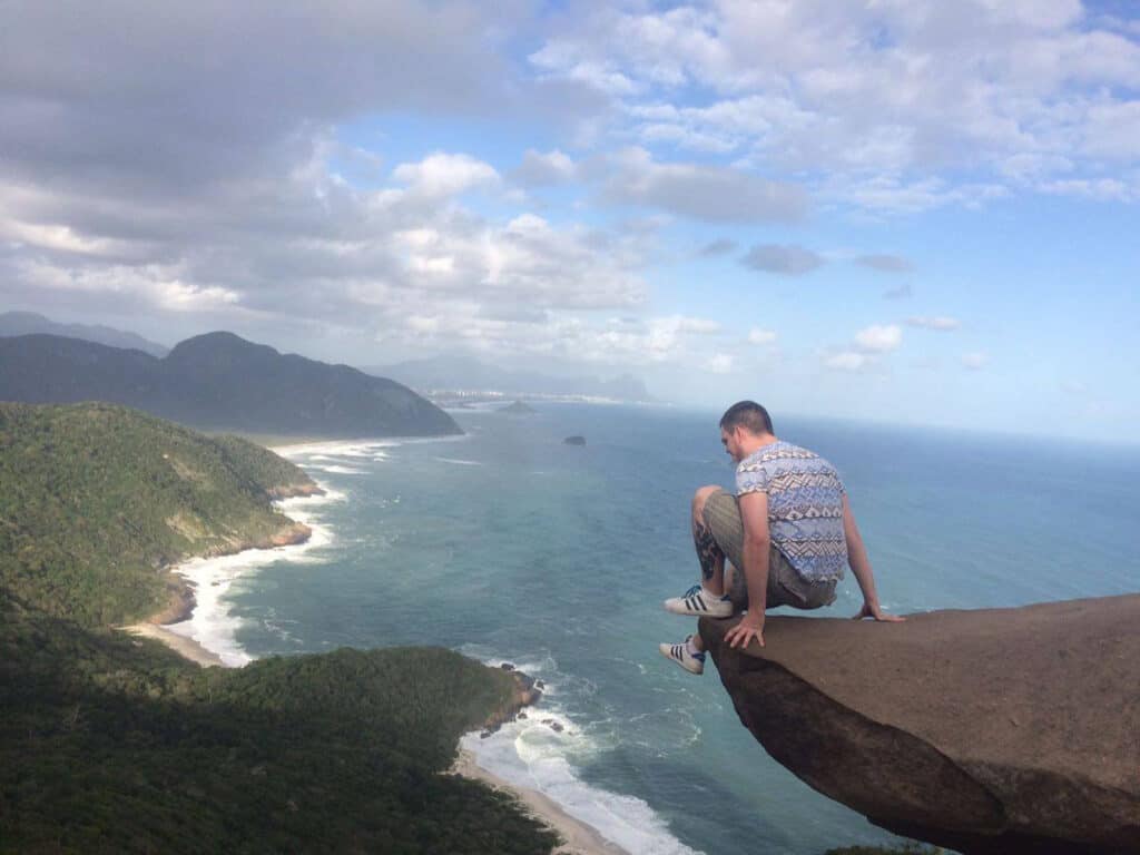 Young man sitting on a cliff overlooking the ocean and lush green coastline in Berlin.