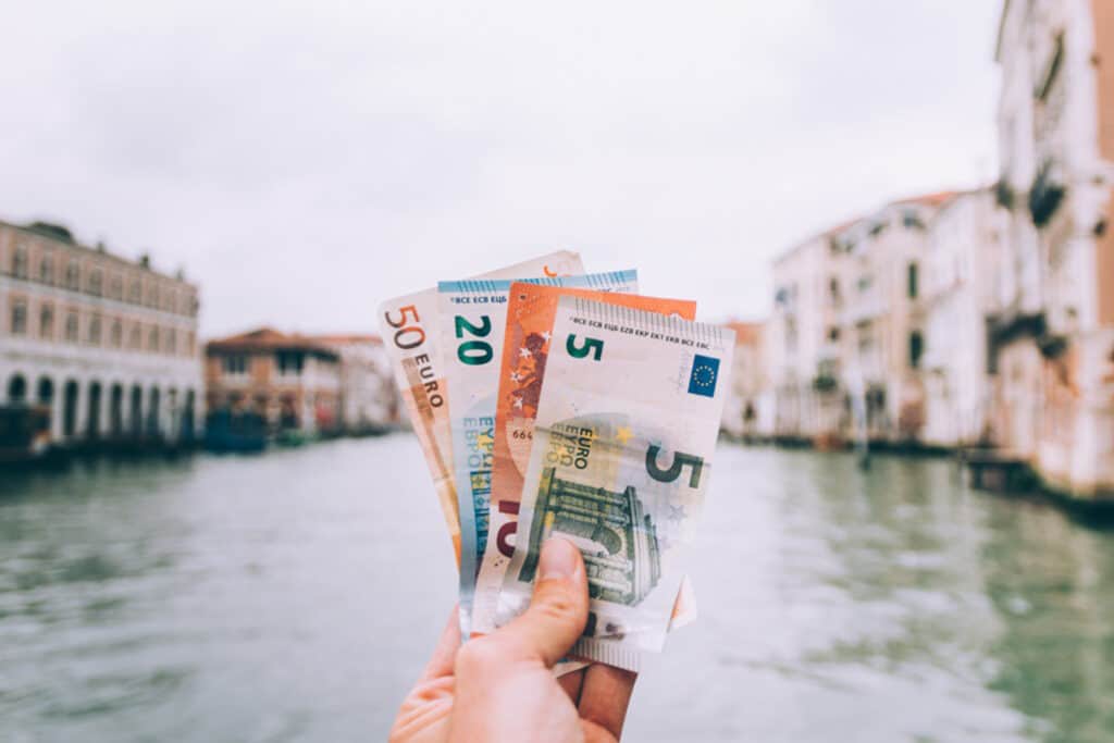Hand holding euro banknotes in front of Berlin canal with historic buildings.