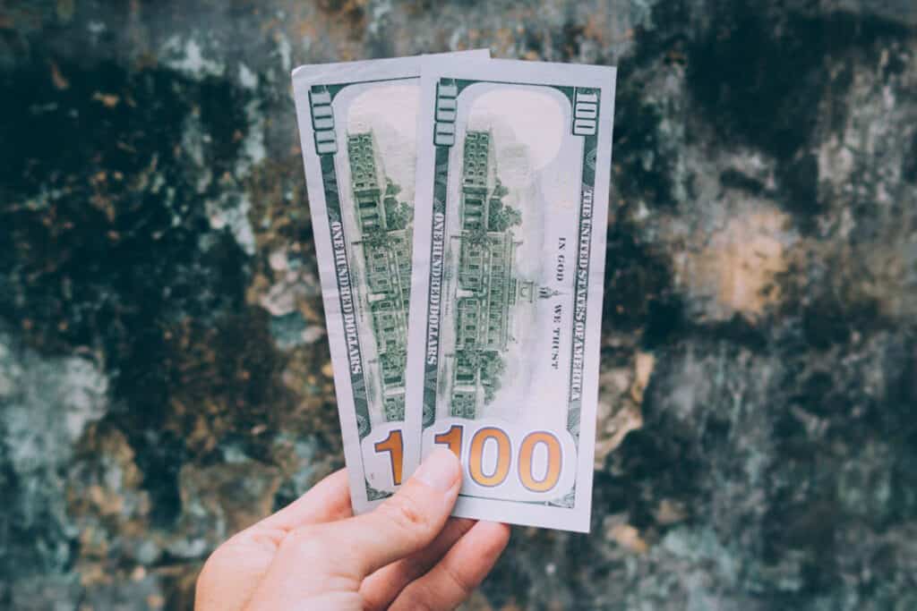 US dollar bills held in hand, showcasing currency notes in front of a rocky backdrop.