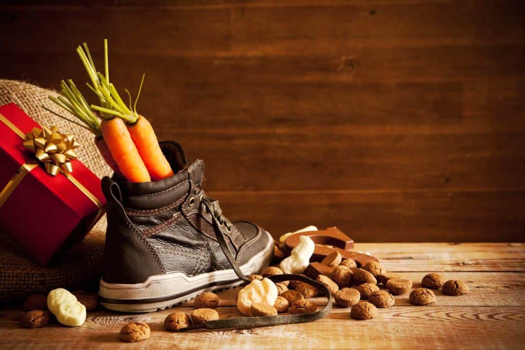 Festive shoe filled with carrots, surrounded by nuts and chocolates, on a wooden surface for holiday.