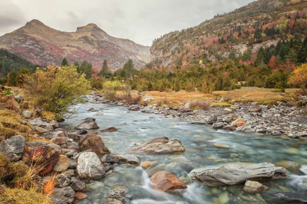 Beautiful mountain river flowing through a lush valley with colourful autumn trees and rocky terrain.