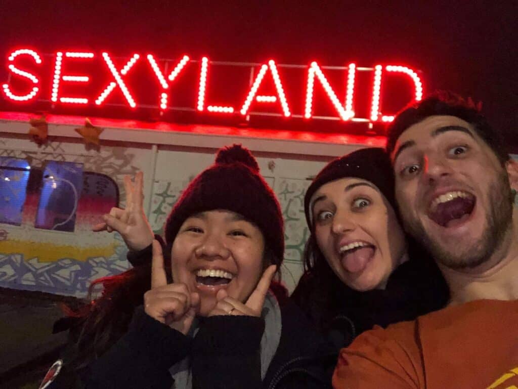 Vibrant group of friends enjoying nightlife at Mitte Hostel, Berlin, with neon "SEXYLAND" sign in th.