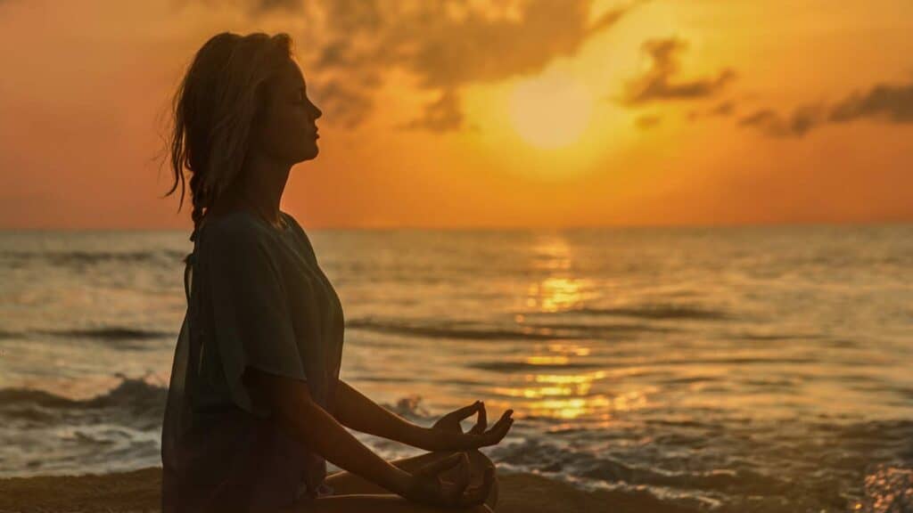 Sunset over the Baltic Sea with a silhouette of a woman meditating on the beach.