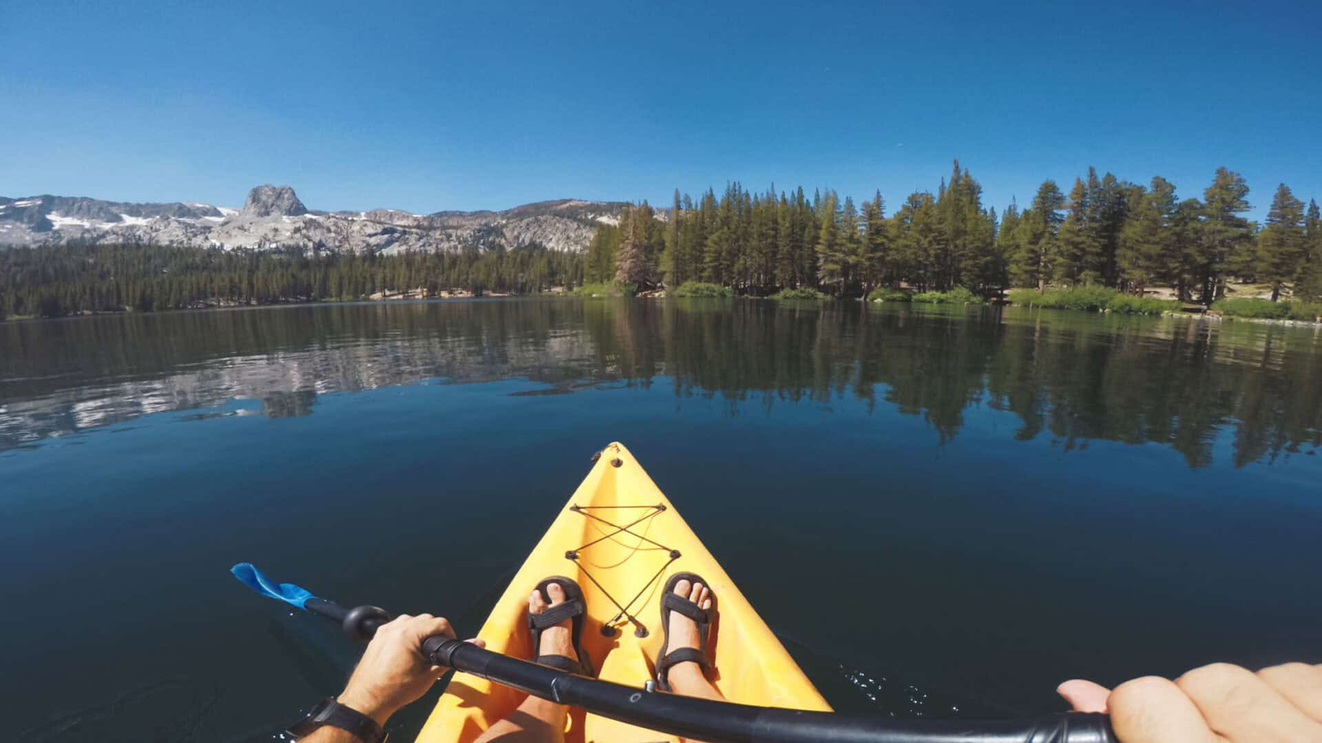 Scenic view of a person kayaking on a calm lake near Mitte Hostel, Berlin, with mountains and forest.