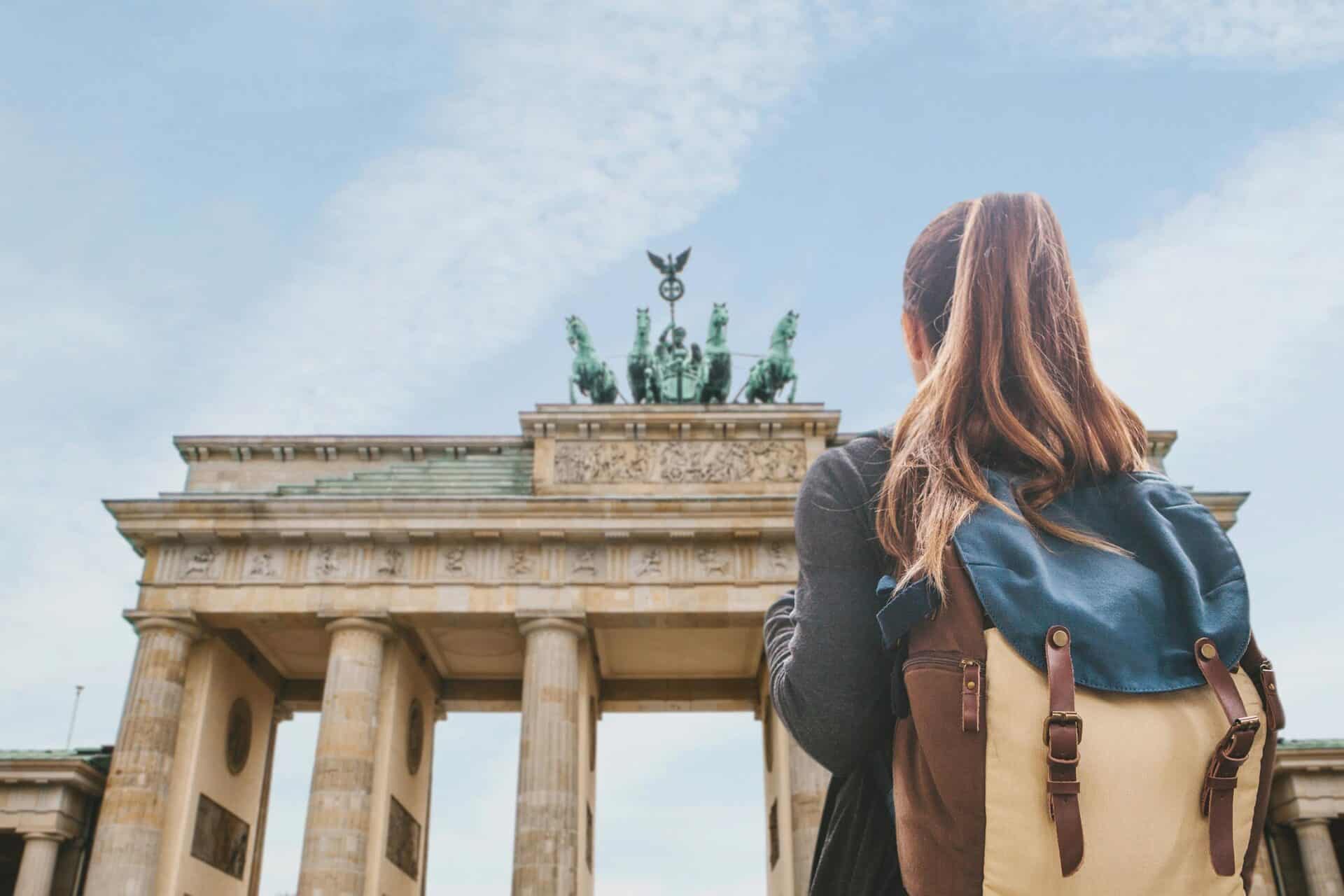 Brandenburg Gate in Berlin, a popular tourist attraction, viewed by a woman with a backpack.