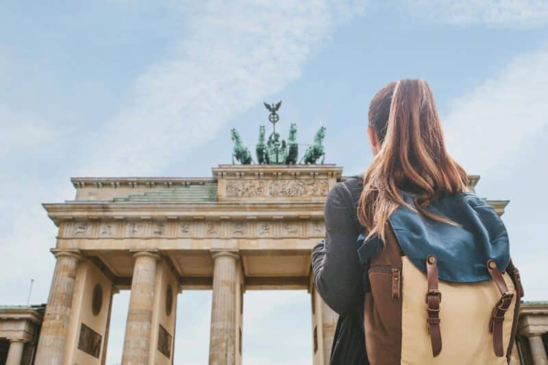 Brandenburg Gate in Berlin, a popular tourist attraction, viewed by a woman with a backpack.