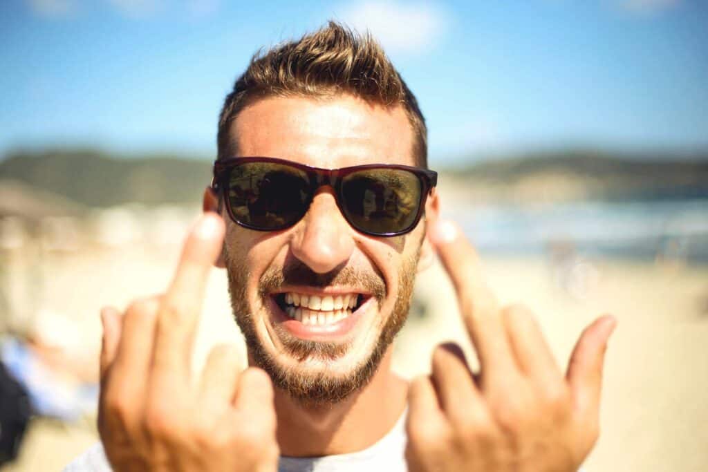 Young man smiling at the beach in Berlin, wearing sunglasses, enjoying sunny weather.