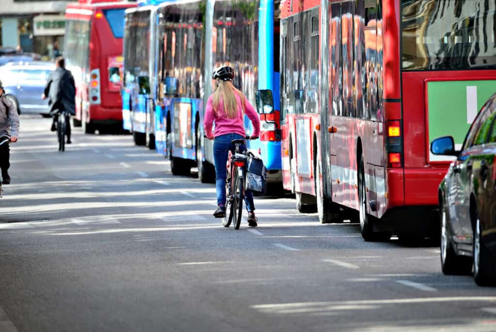 Cyclist waiting at a bus stop in Mitte, Berlin, with buses and pedestrians nearby.