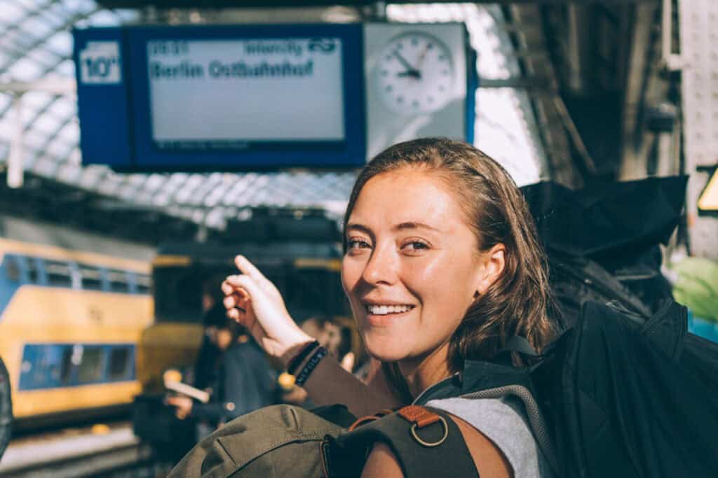 Young woman with backpack at Berlin Central Station, smiling and pointing.