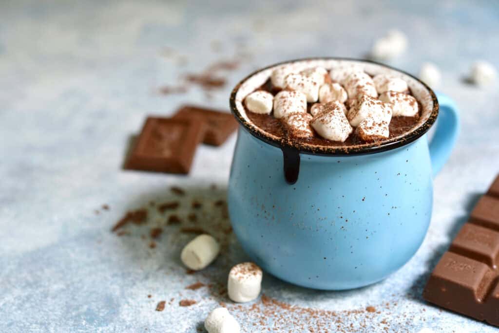 Hot chocolate with marshmallows in a blue mug, surrounded by chocolate pieces and cocoa powder. Perf.