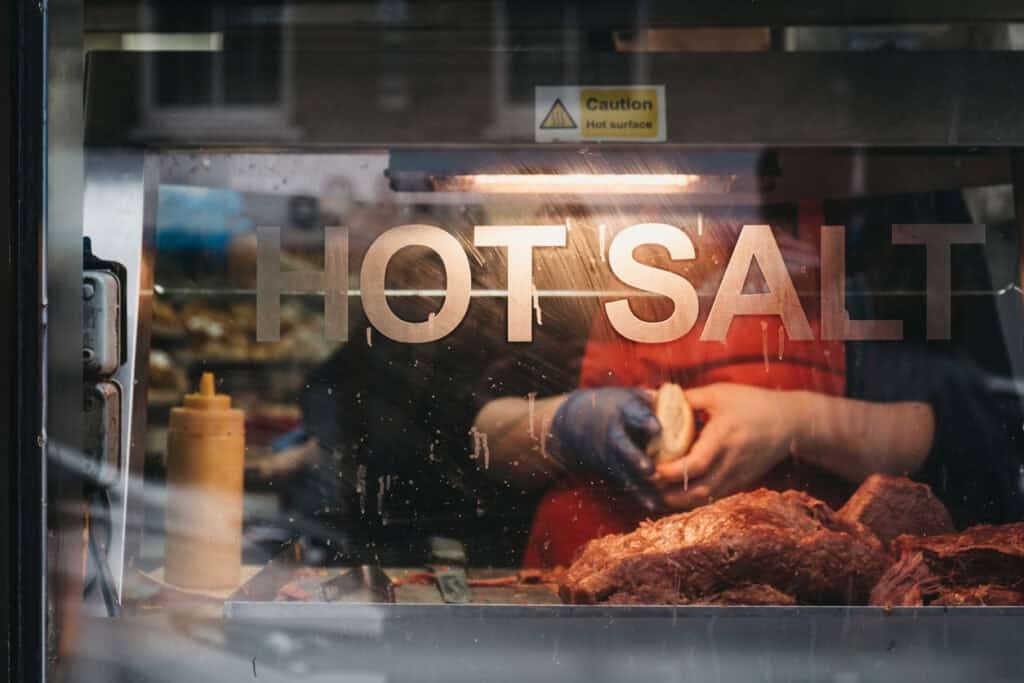 Hot salt seasoning being applied to meat in a professional kitchen.