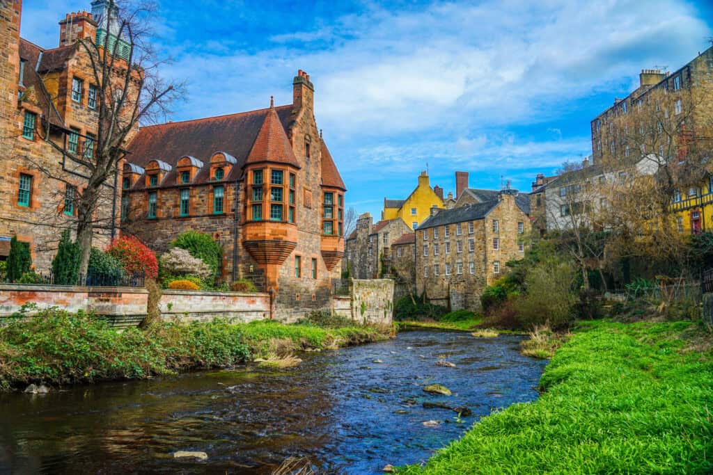 A historic building with a turret and colourful rooftops beside a flowing river.