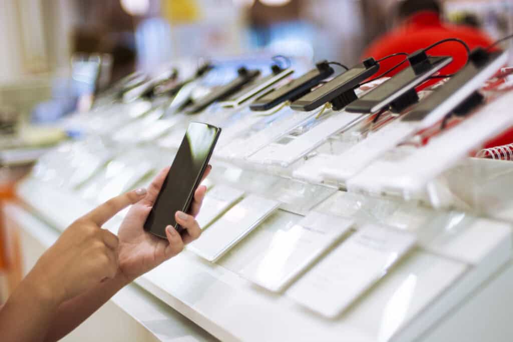 Smartphone in hand browsing mobile phones at electronics store display.