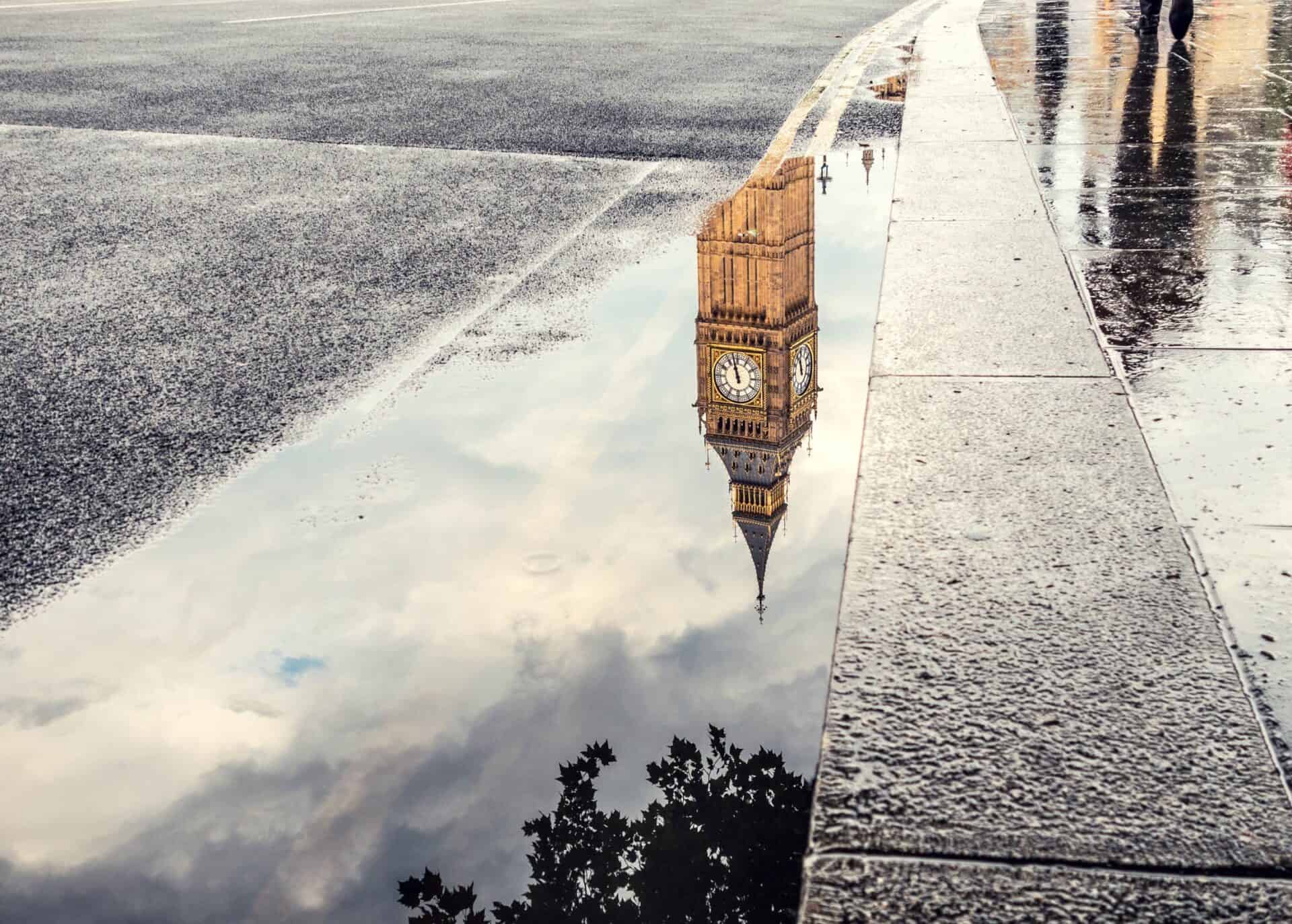 Big Ben clock tower reflection in a puddle on a rainy street in London.
