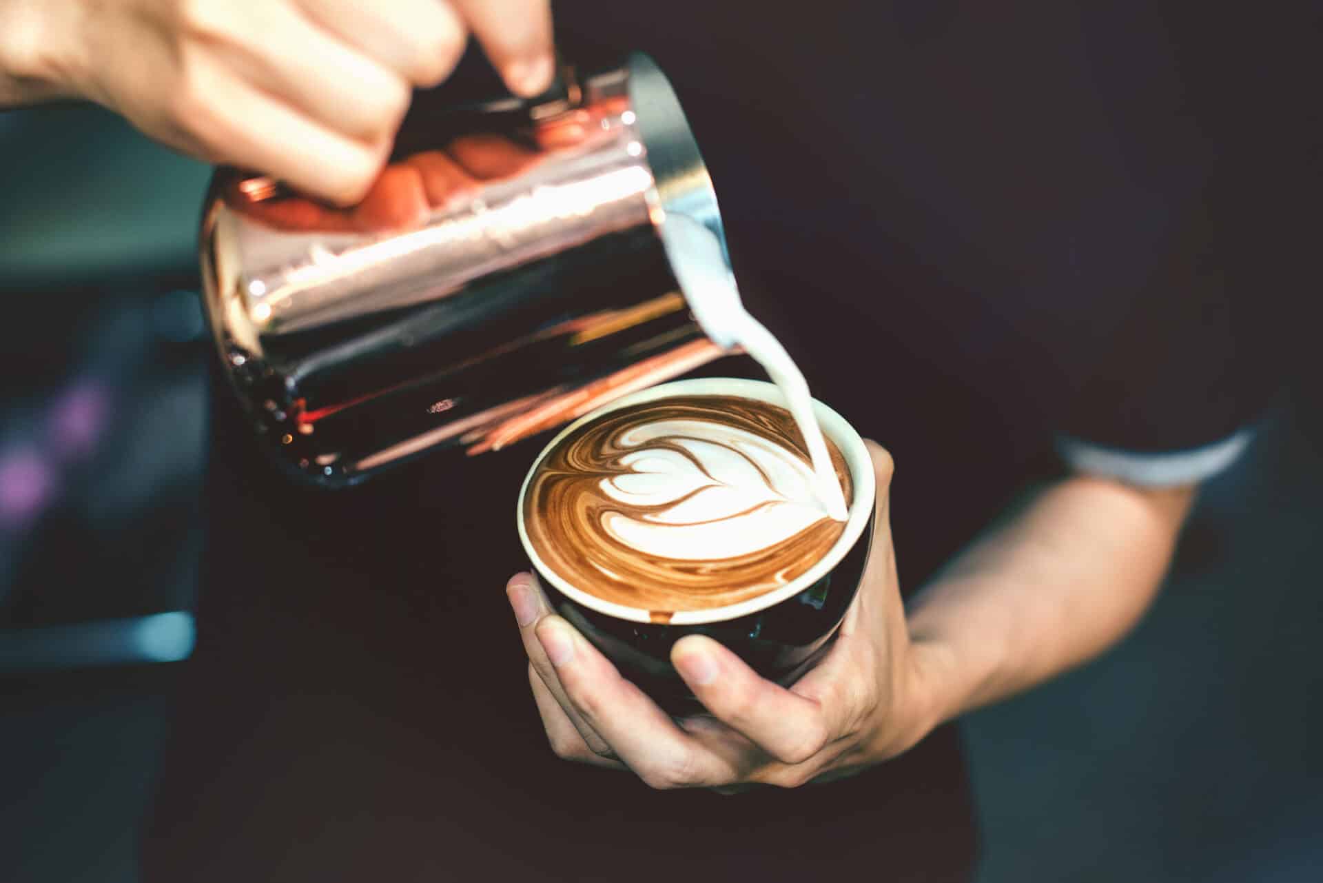 Barista pouring milk into a cup of latte with latte art in Berlin, Germany.