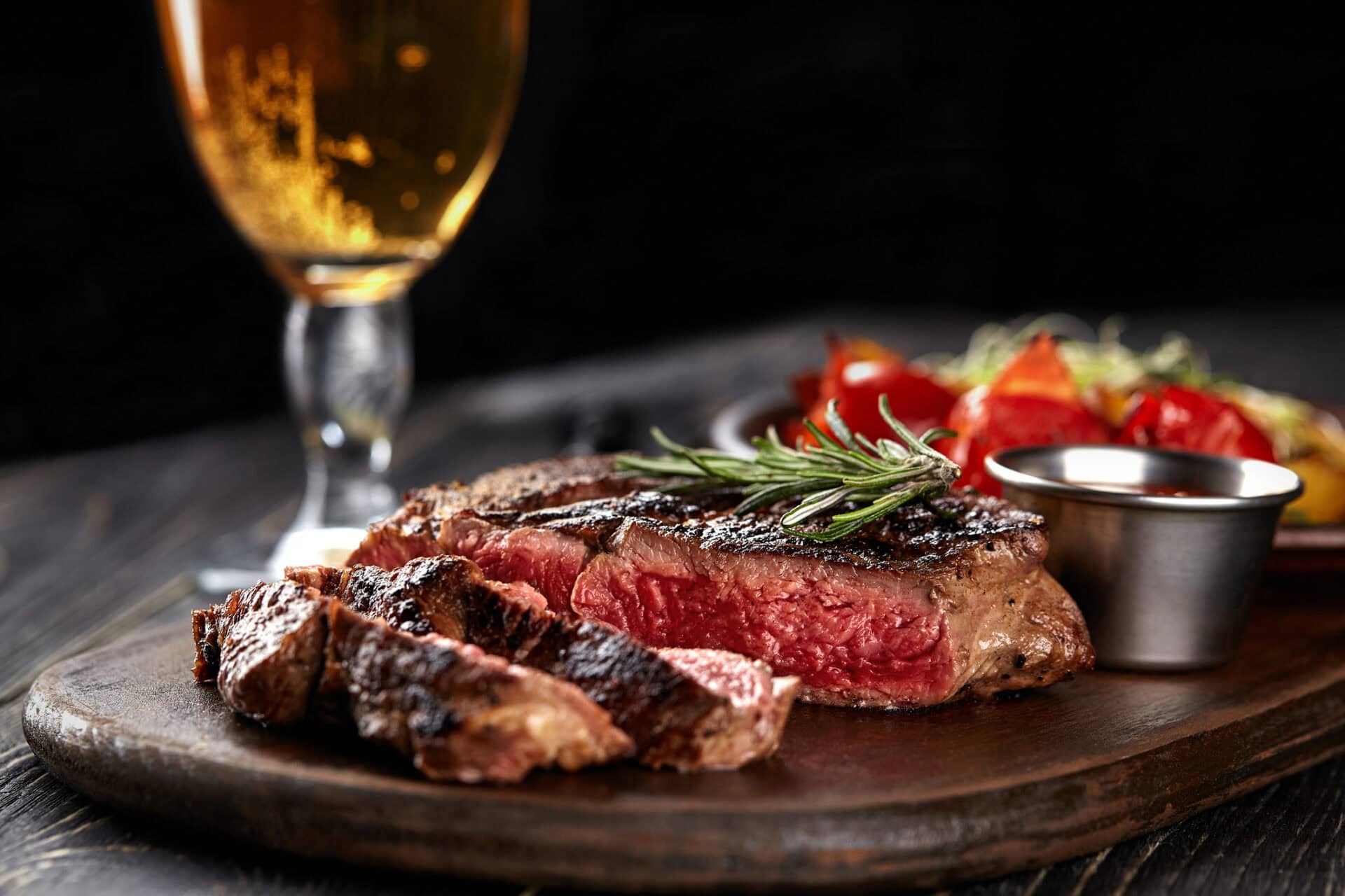 Juicy grilled steak served with fresh salad and a glass of beer on a wooden board.