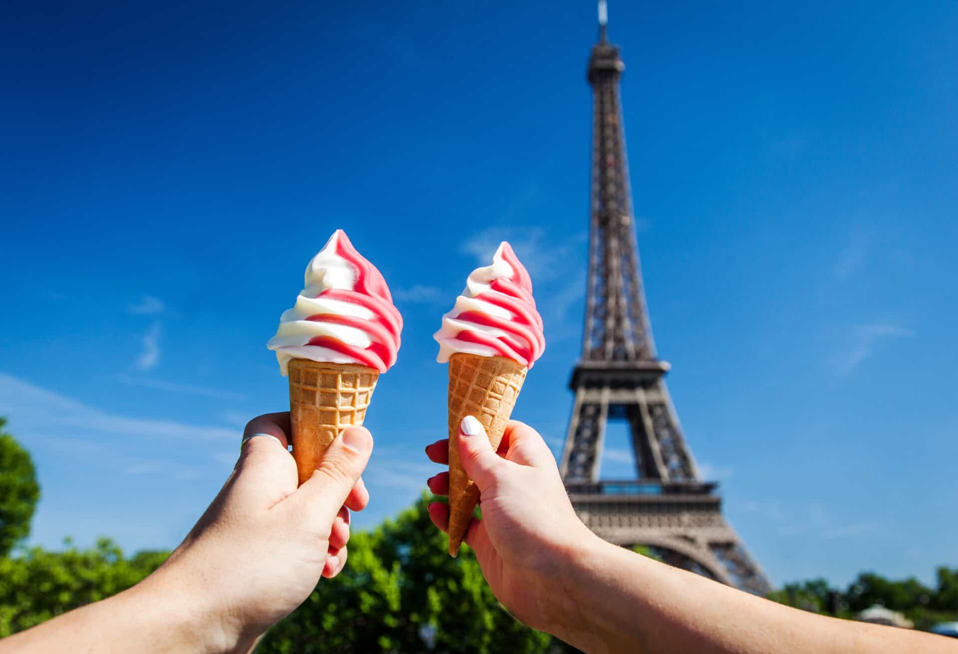 Eiffel Tower with two hands holding ice cream cones in front, sunny day in Paris.