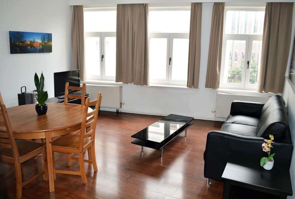 Modern hostel lounge with wooden dining table, black sofa, and large windows in Berlin.
