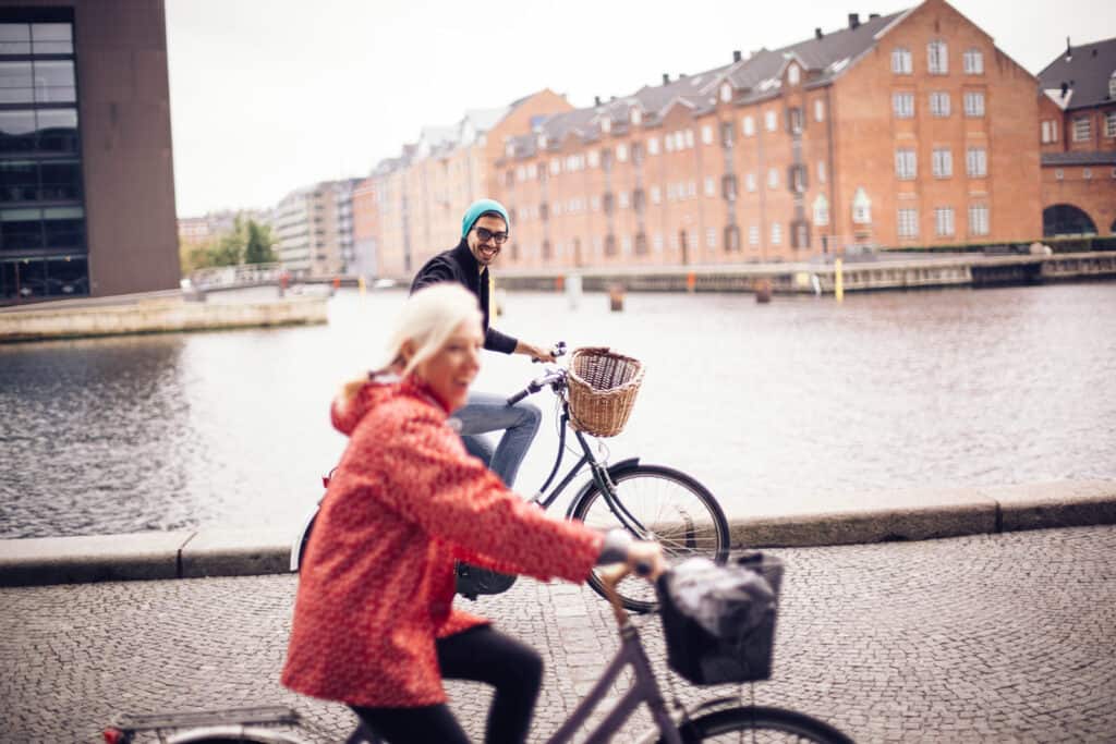 Two people cycling along the river in Berlin near Mitte Hostel, with historic buildings in the backg.