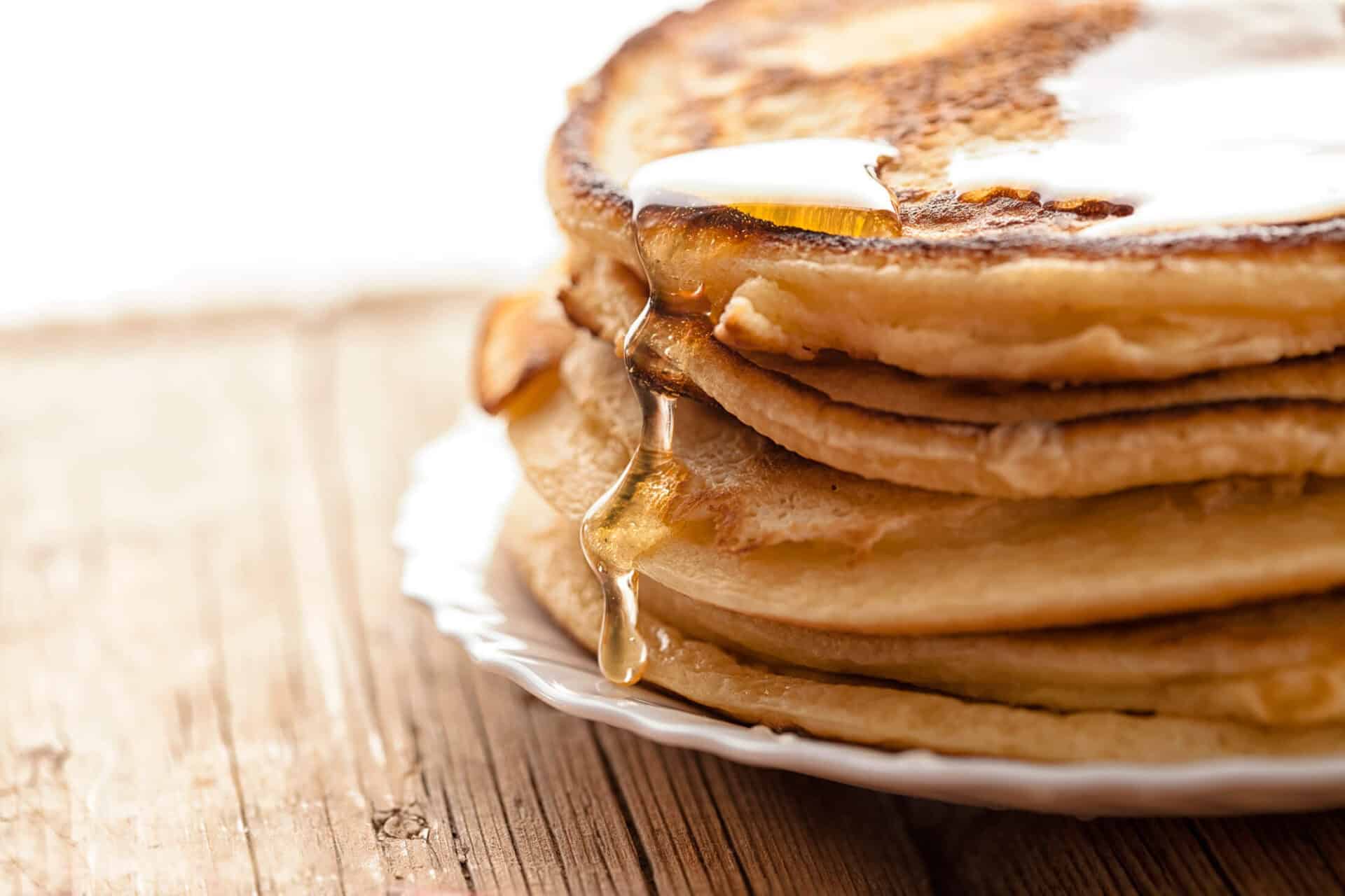 Pancakes drizzled with syrup and topped with a lemon wedge on a white plate.