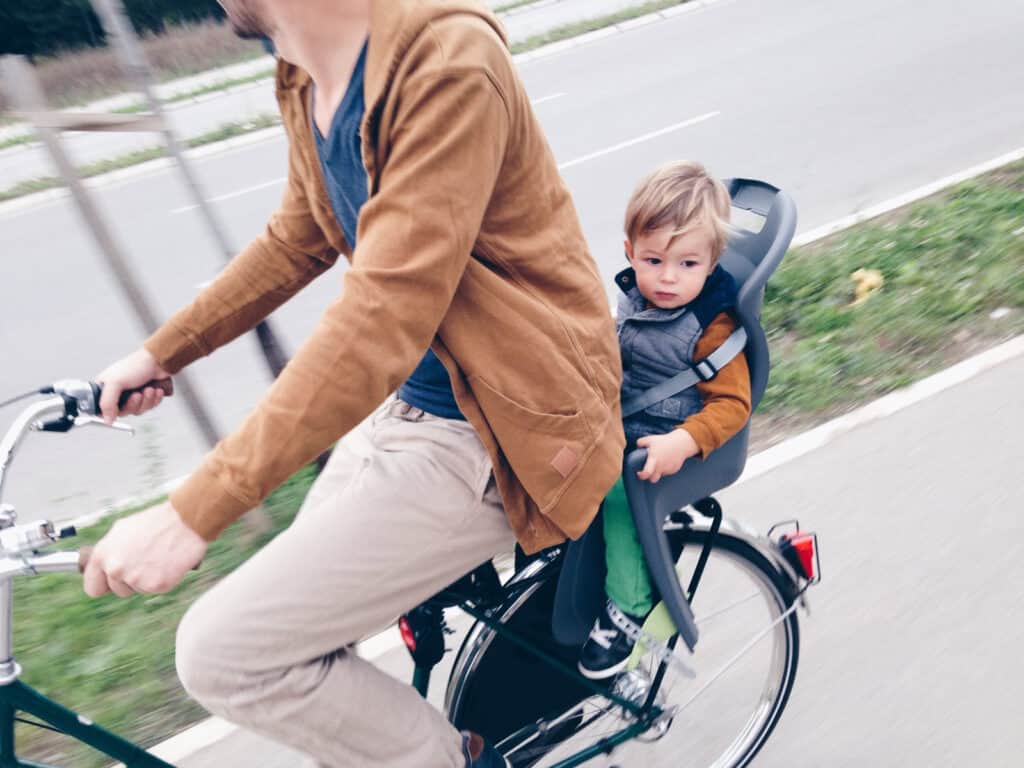Family cycling with a young child in a child seat on a city bike in Berlin Mitte.