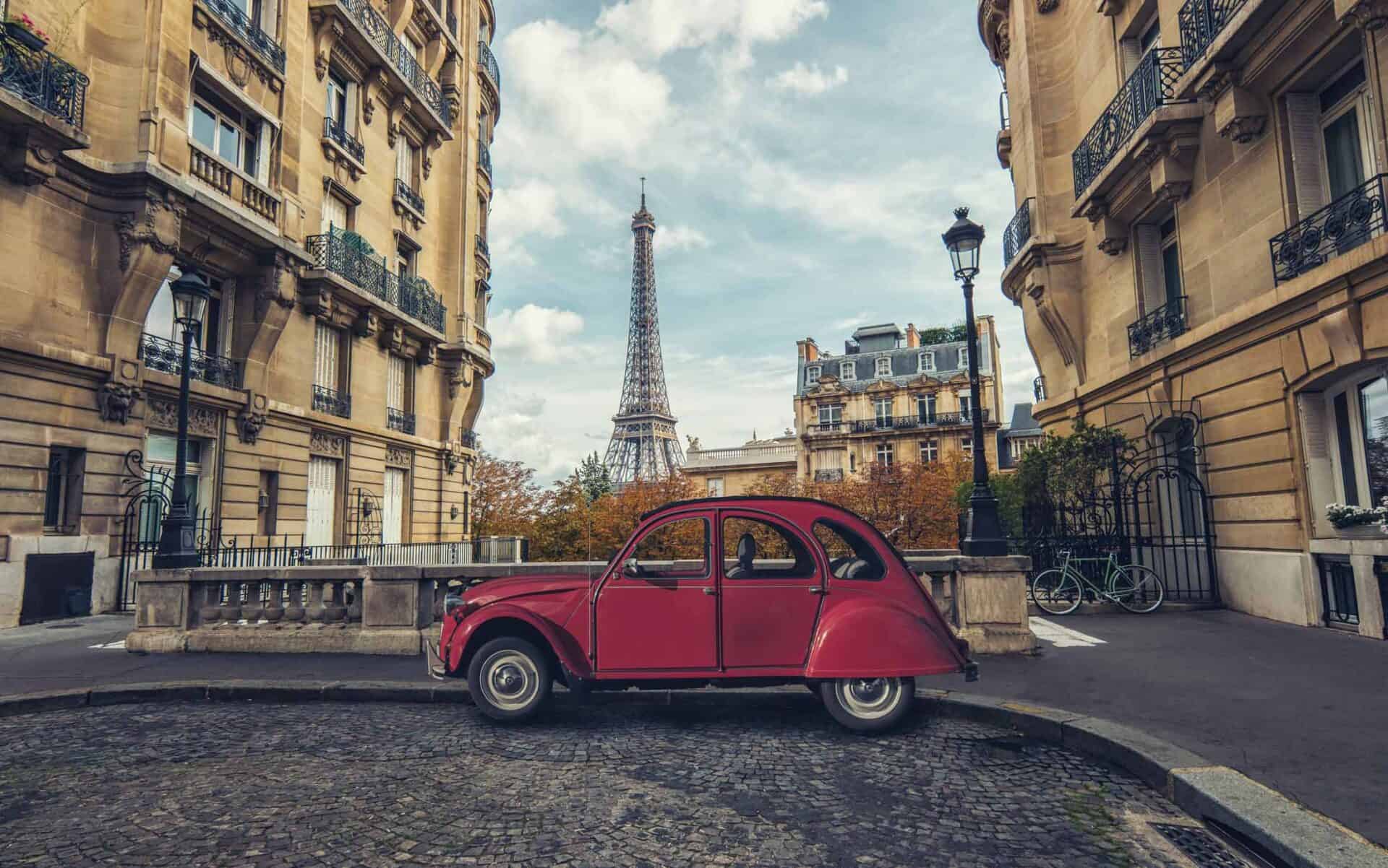 Red vintage Citroën 2CV car parked on a cobbled street in Paris with classic architecture and the Ei.